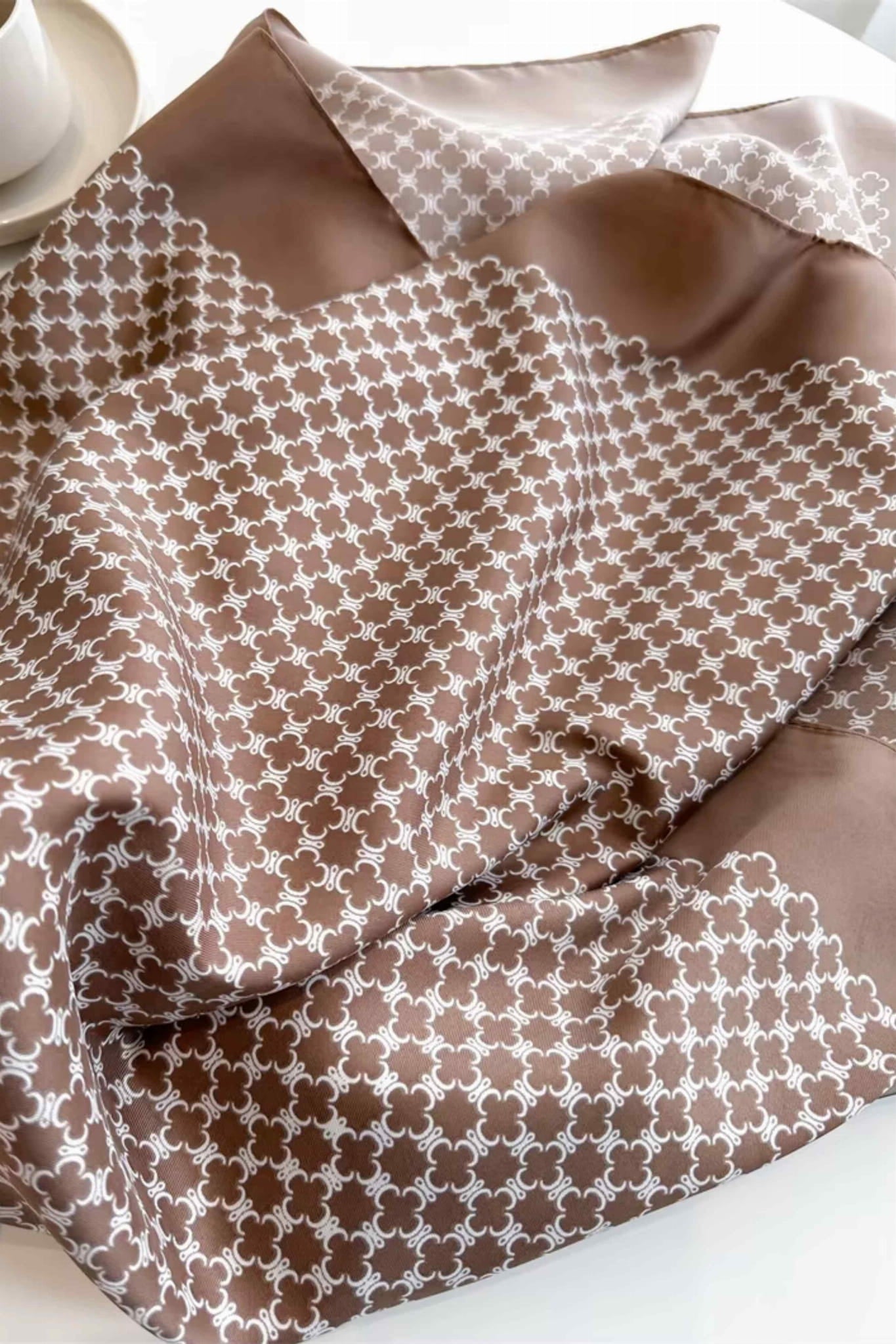 Brązowa apaszka z białym wzorem leżąca na stole, prezentująca swoje wymiary 90x90 cm | KAMEA | Spironik.pl