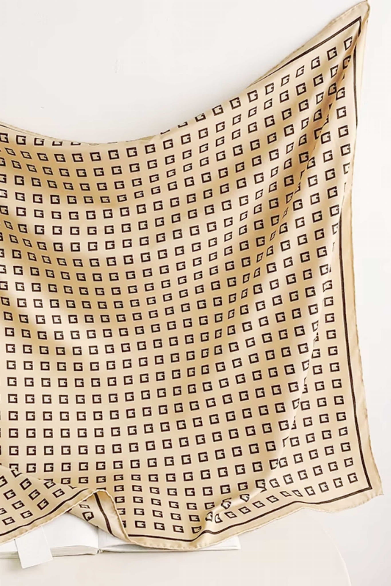 Detal satynowej tkaniny apaszki w beżowym kolorze z regularnym czarnym wzorem | KAMEA | Spironik.pl