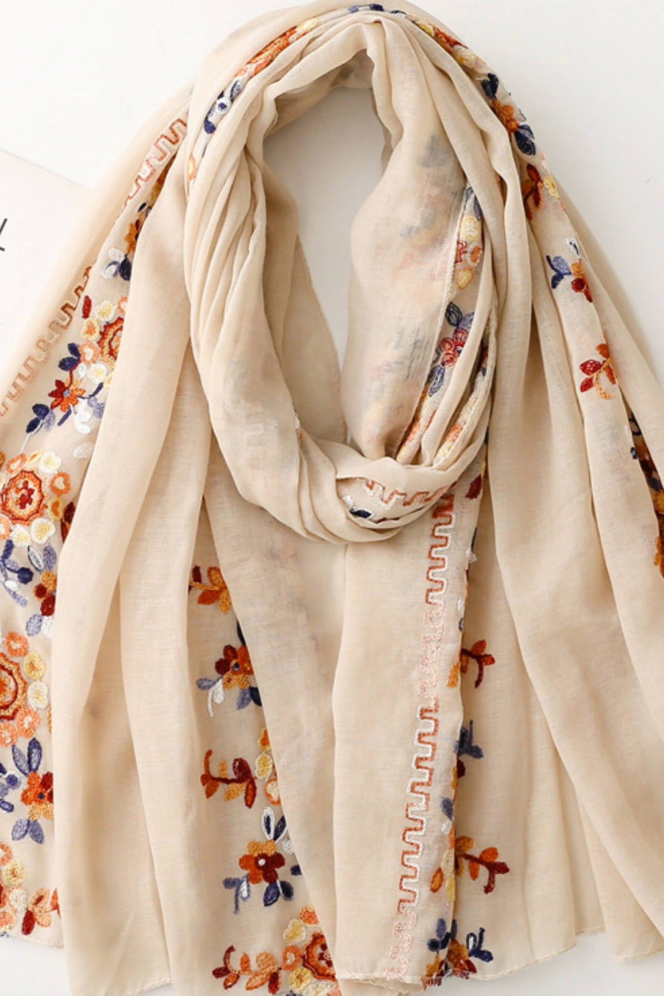 Detal haftu kwiatowego na beżowym szalu, ukazujący kolorowe wzory i delikatną fakturę materiału | KAMEA | Spironik.pl