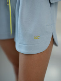 Kurze Jogginghose mit Falten – elastischer Bund und dekorativer Kordelzug. Farbe: Himmelblau (gelbe Schrift).