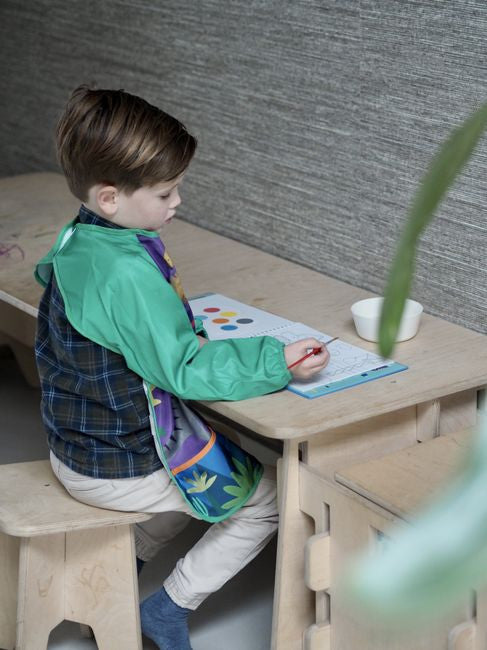 Fartuszek dinozaurów na tle kreatywnego miejsca zabaw, zachęcający do twórczości | Floss & Rock | Spironik.pl